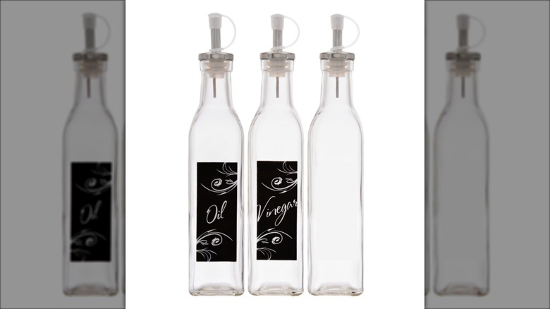 Three clear glass oil and vinegar bottles with metal pour spouts on a white background