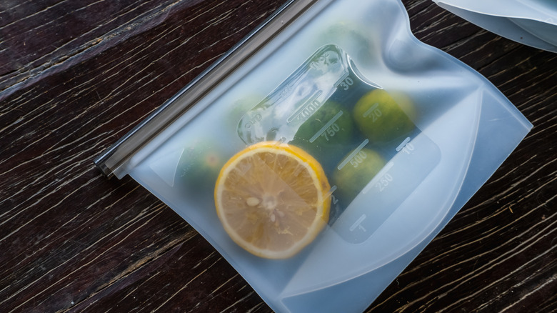 a reusable snack bag containing a sliced lemon and citrus fruits lying on top of a wooden surface