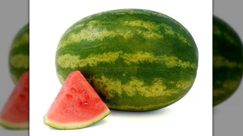 Whole intact watermelon with a single triangular slice in the foreground.