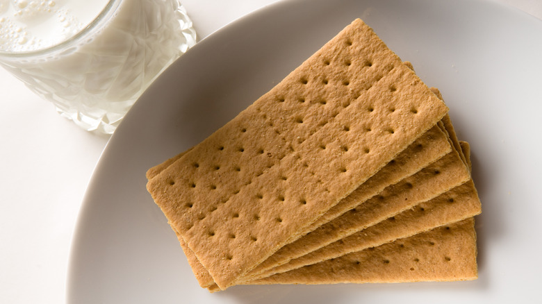 Stack of graham crackers on white plate next to milk