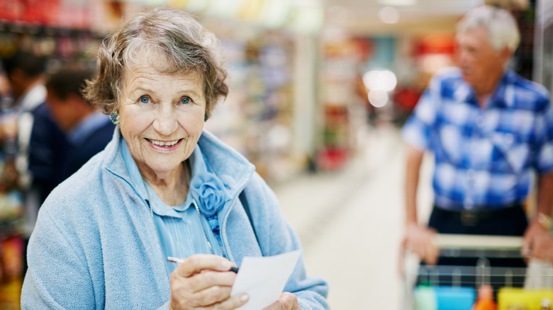 older woman with pen and paper for list and older man guiding grocery cart