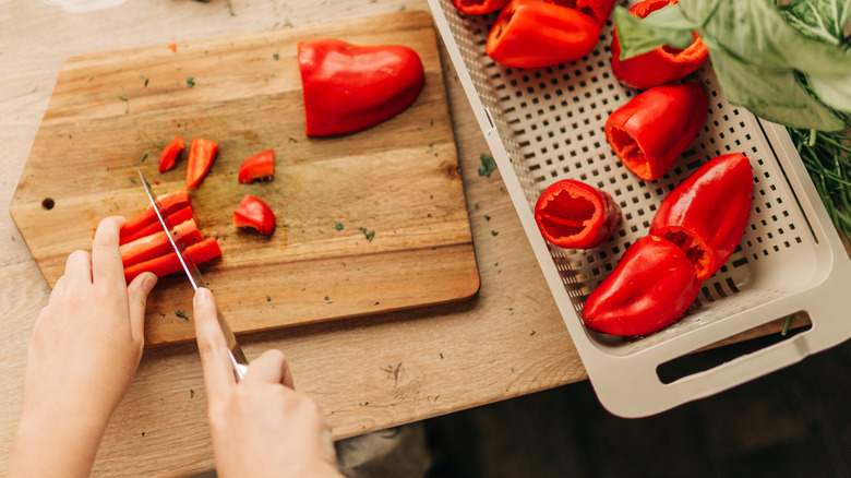 hands cutting bell peppers on wooden board