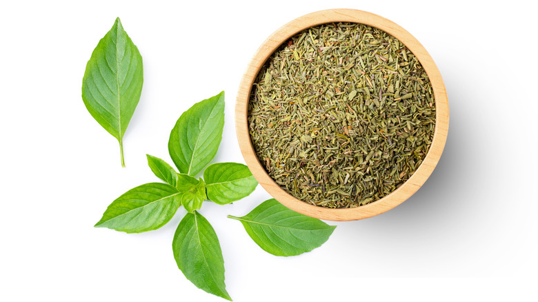 bowl of dried basil alongside fresh basil leaves