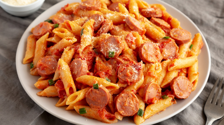 Sliced hot dogs, tomatoes, and penne pasta in a dish