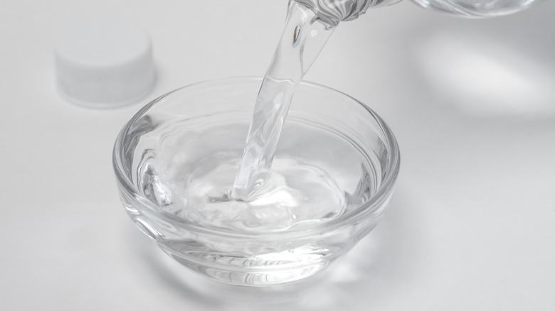 Bottle pouring white vinegar in a bowl