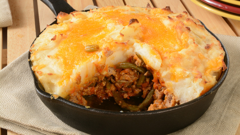 Hamburger pie in a cast iron skillet with a slice missing