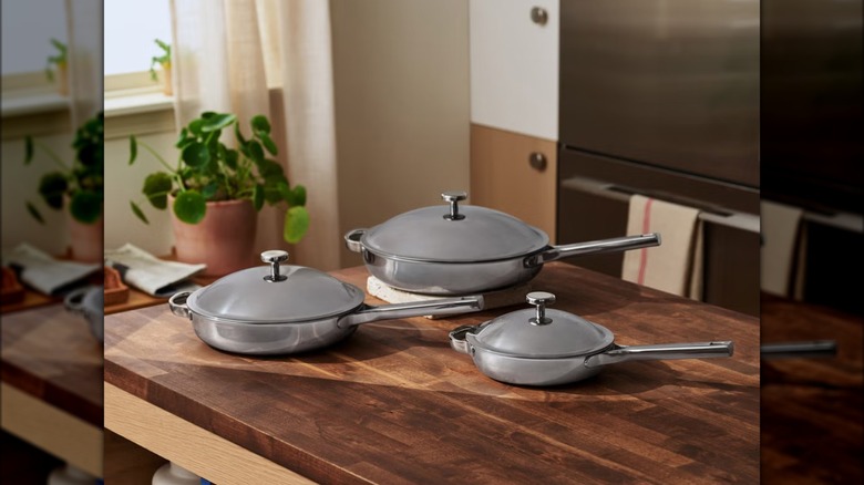 Three differently-sized skillets on a wood table in kitchen.