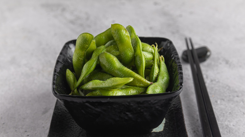 edamame in black bowl next to a set of chopsticks