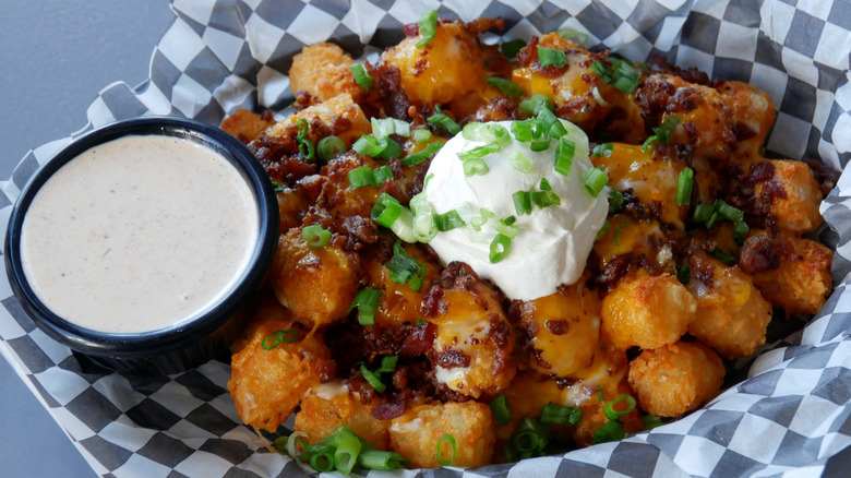 loaded tater tots in basket with chives and sour cream with side of dipping sauce