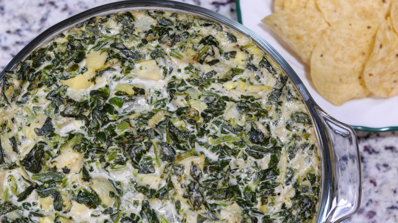 spinach artichoke dip in glass bowl with tortilla chips on side