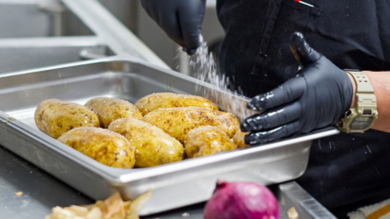 A chef sprinkling Atlantic potatoes with salt on a baking pan