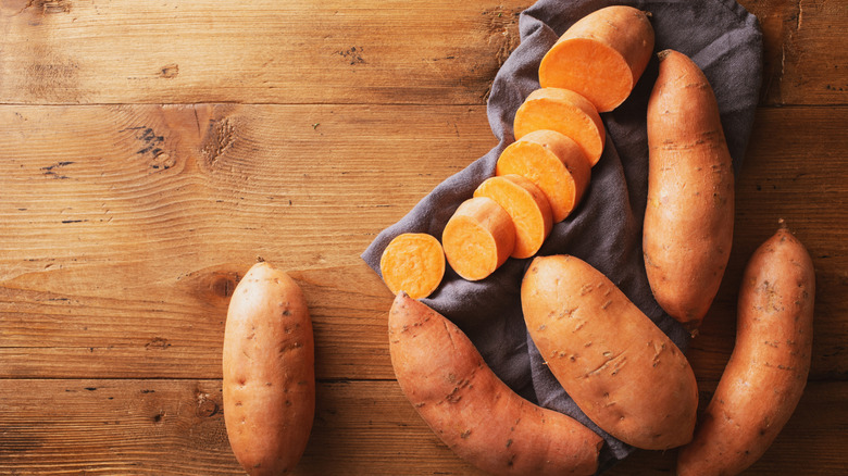 Sweet potatoes on a wooden table with one sliced on a napkin