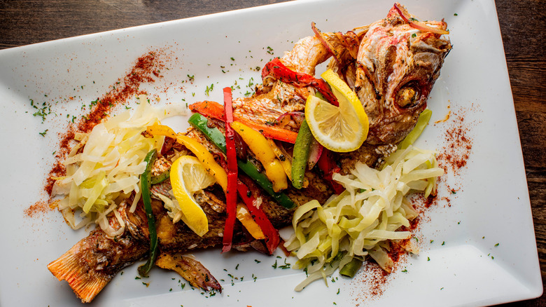 A whole cooked red snapper garnished with lemon and chopped vegetables