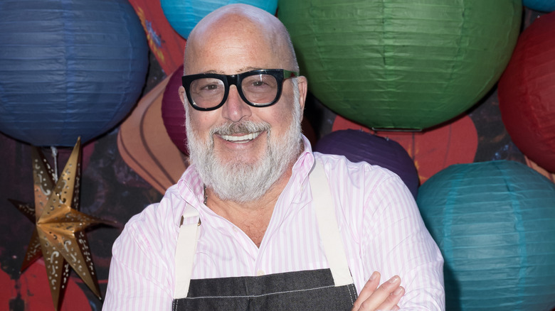 Chef Andrew Zimmern standing in front of lanterns with his arms crossed and smiling