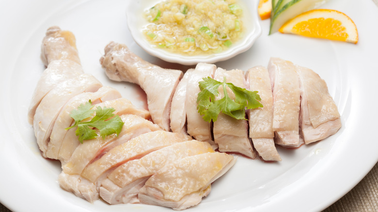 Poached chopped chicken legs garnished with fresh herbs served with a ginger sauce and sliced orange