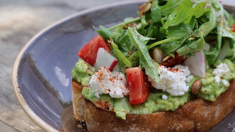 Avocado on ciabatta toast with ricotta, arugula, radishes, tomato