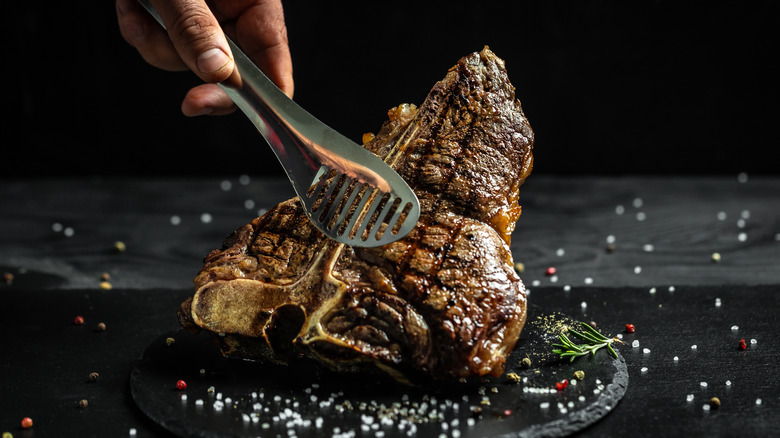 Tongs holding grilled steak