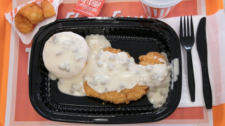 Whataburger gravy on a biscuit and chicken in a plastic black tray with  a side of hashbrowns, ketchup, and coffee