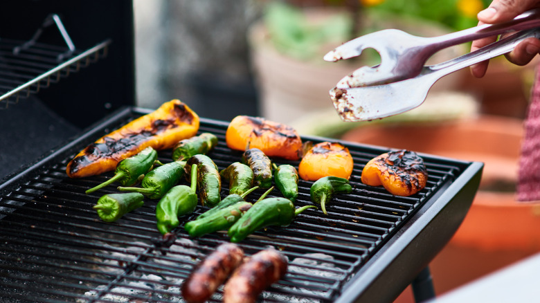Person cooking whole peppers and sausages on grill