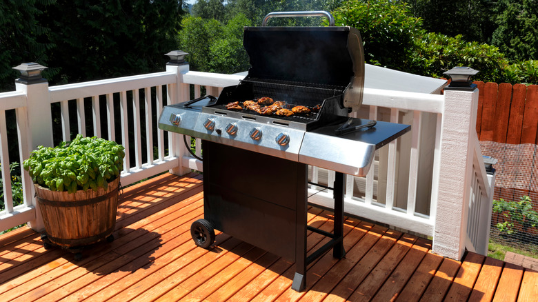 Open grill with chicken pieces on sunny deck