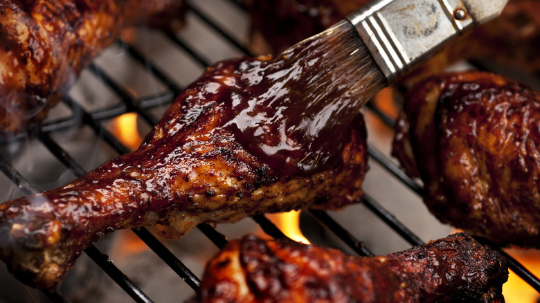 Brush glazing chicken drumstick on grill