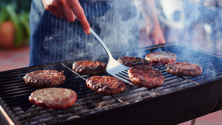 Person cooking burgers on outdoor grill