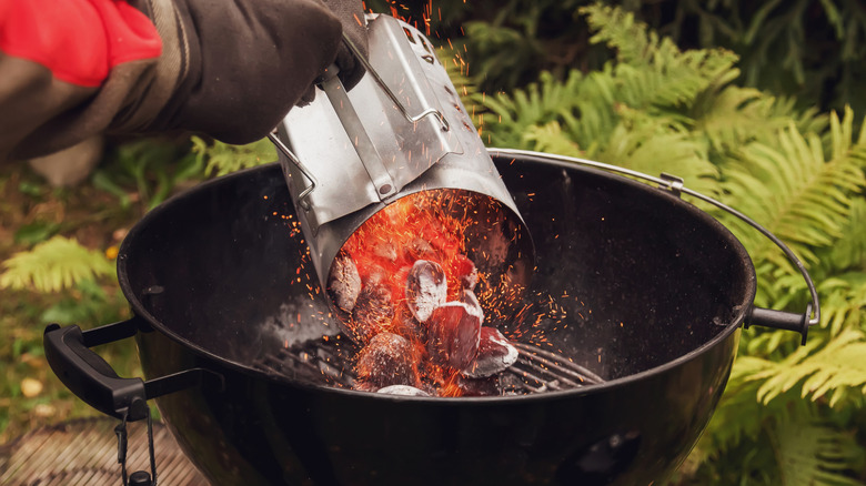 Gloved hand pouring coals from chimney starter into charcoal grill