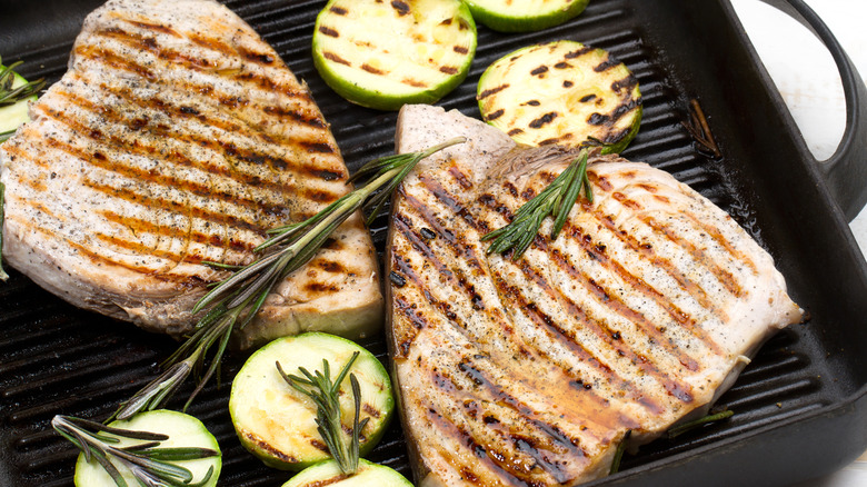 Two swordfish steaks on grill with sliced zucchini and rosemary