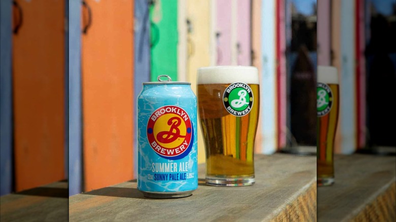 Light blue can of Brooklyn Bewery summer ale next to a filled pint glass on a boardwalk