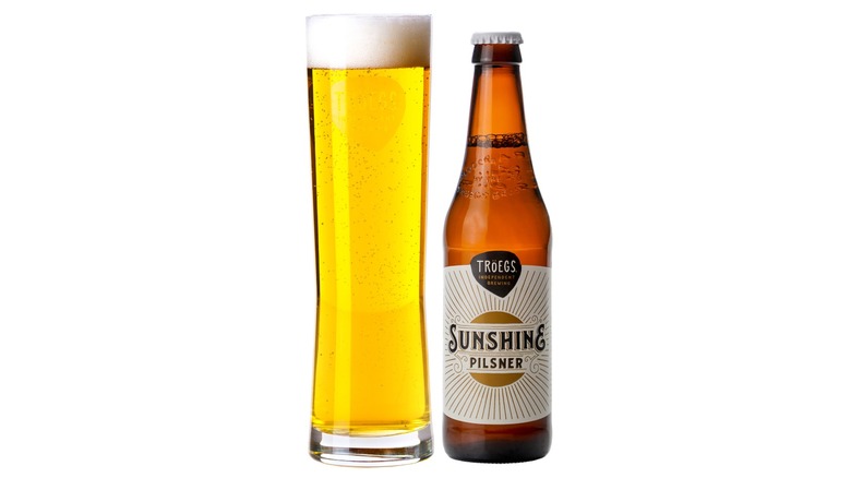Bottle of Troegs Sunshine Pilsner next to a full pint glass of beer on a white background