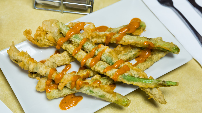 battered asparagus on plate with sauce drizzle