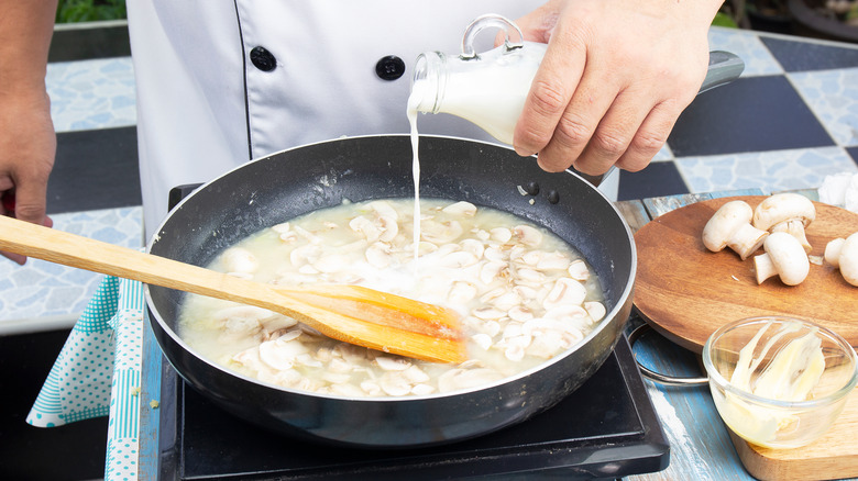 chef pouring milk or cream into a pan for mushroom soup