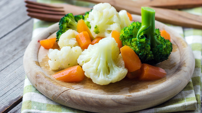 Steamed carrots, broccoli, and cauliflower on wooden board