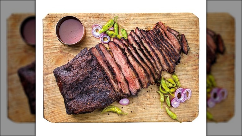 Sliced barbecue brisket on wood cutting board against white background.