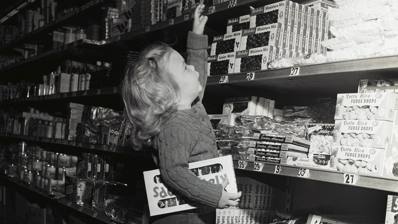 A little girl from the '50s shopping in the candy aisle in black and white