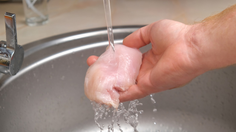 A person rinsing raw chicken breast
