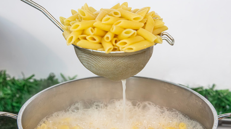 Draining cooked penne and reserving the pasta water