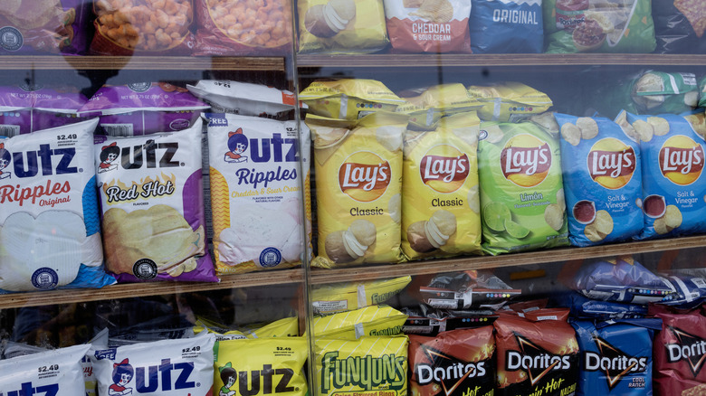 A variety of potato chip bags lined up on shelves at the grocery store