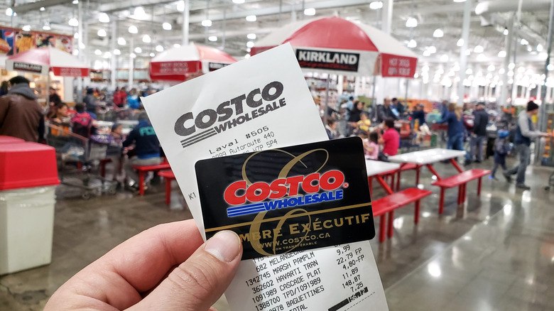 Costco shopper holding up card and receipt inside store.