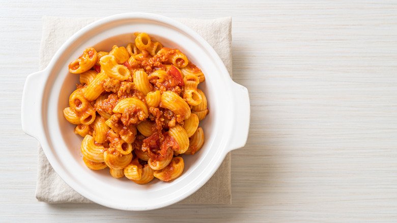 American chop suey in a white dish with a white napkin and white table background.
