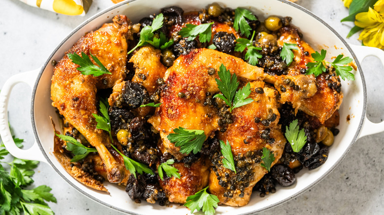Prepared chicken Marbella with chopped parsley garnish in a casserole dish.