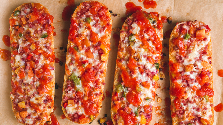 Four French bread pizzas with diced toppings, cheese and sauce on brown butcher paper.