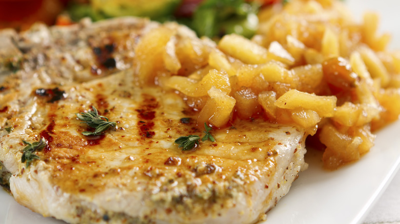 Close up of pork chops with applesauce served on a white plate.