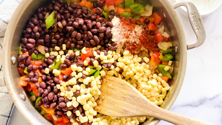 A can of green enchilada sauce next to a glass bowl of corn and a wooden spoon