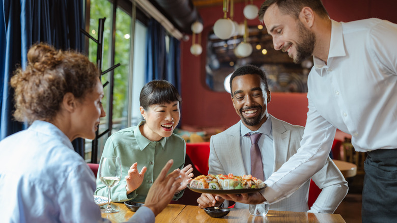 Smiling, excited people being served a platter of sushi at restaurant