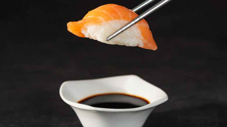 Piece of nigiri held with chopsticks over dish of soy sauce, about to be dipped