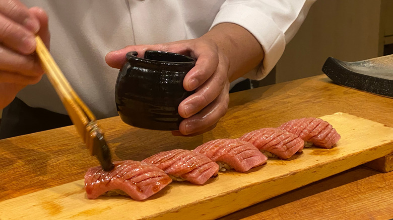 Chef brushing sushi with soy sauce on wooden serving board