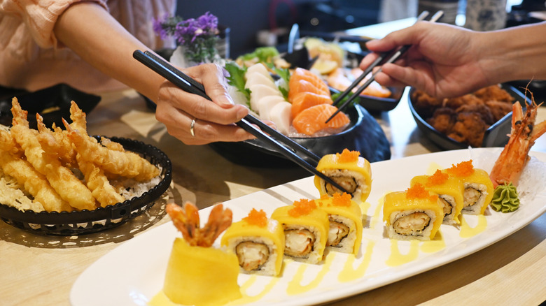 Hands holding chopsticks, picking up pieces of sushi