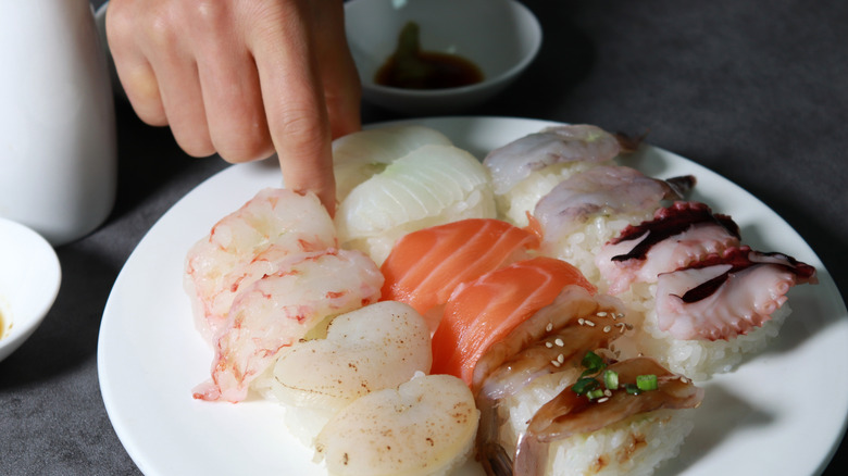 Hand shown picking up sushi from a plate with many types of nigiri