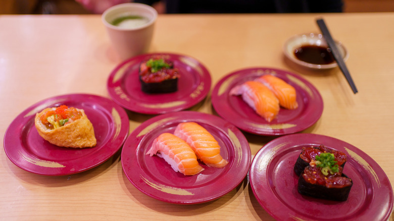 Nigiri, gunkan, and inari sushi on small plates on wooden table